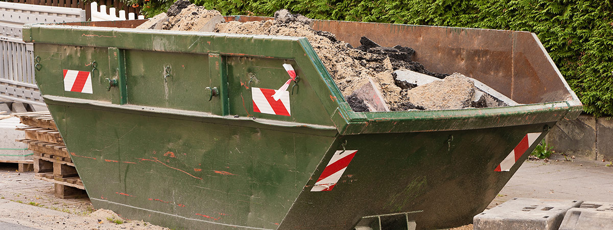 Ein grüner Container mit Bauschutt vor einer grünen Hecke